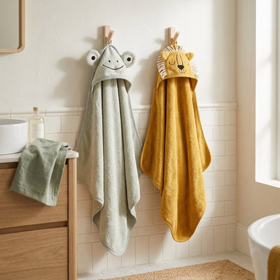 Capes de bain grenouille vert d'eau et lion moutarde suspendues à des patères de salle de bain