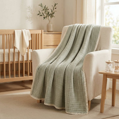 Couverture bébé en gaze de coton vert sauge à bordure dentelle posée sur un fauteuil