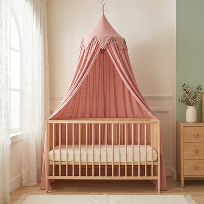 Ciel de lit en voile vieux rose à pompons suspendu au-dessus d'un lit à barreaux en bois