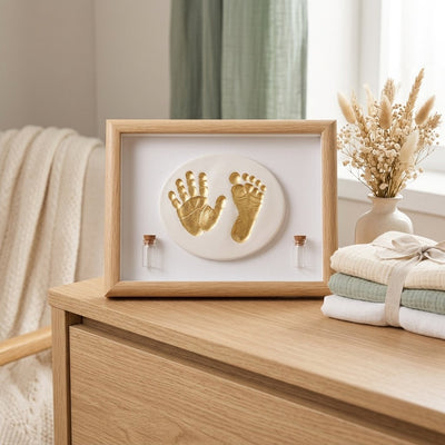 Cadre empreinte bébé main et pied dorés avec deux fioles, posé sur une commode en bois