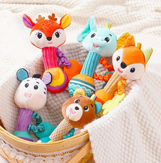 5 Doudou bébé hochet cerf, zèbre, éléphant, ours, renard orange rose violet blanc, bleu, vert, marron, noir et jaune avec anneau de dentition en forme de patte posé sur un tissu cranté clair dans un panier macramé et osier Image
