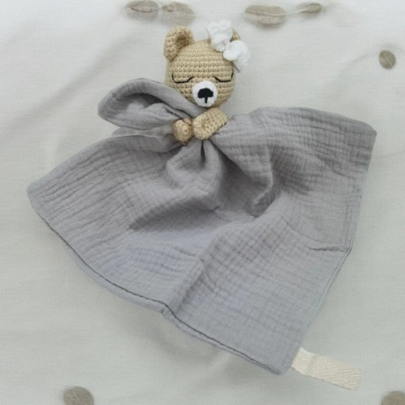 FATIMA est un adorable doudou plat représentant un ours au crochet. Doté d'un noeud blanc sur la tête, il tient un mouchoir ou carré de gaze de coton entre ses pattes pour offrir douceur et réconfort à votre enfant. Disponible en quatre coloris : Écru, Marron, Bleu et Vieux rose. BLEU