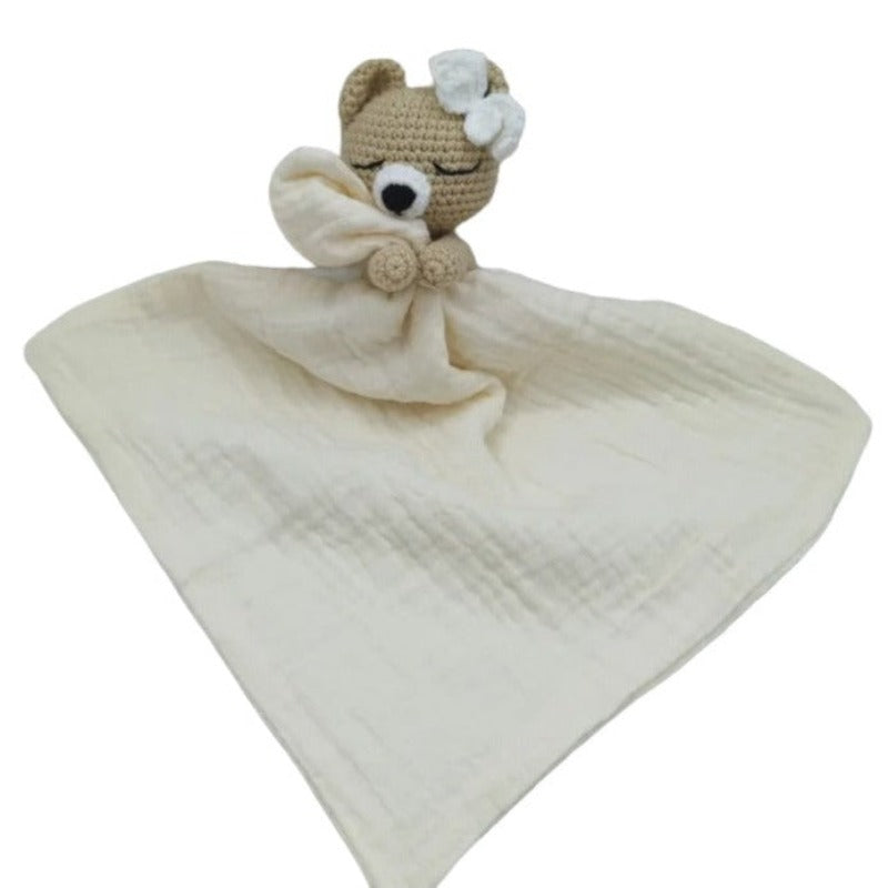 FATIMA est un adorable doudou plat représentant un ours au crochet. Doté d'un noeud blanc sur la tête, il tient un mouchoir ou carré de gaze de coton entre ses pattes pour offrir douceur et réconfort à votre enfant. Disponible en quatre coloris : Écru, Marron, Bleu et Vieux rose.