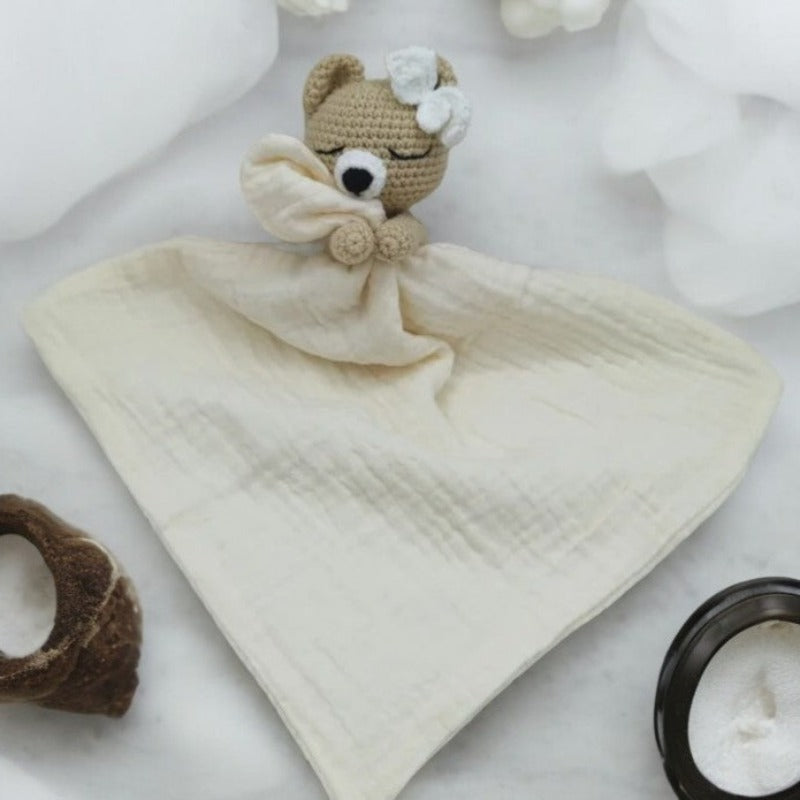 FATIMA est un adorable doudou plat représentant un ours au crochet. Doté d'un noeud blanc sur la tête, il tient un mouchoir ou carré de gaze de coton entre ses pattes pour offrir douceur et réconfort à votre enfant. Disponible en quatre coloris : Écru, Marron, Bleu et Vieux rose. ECRU