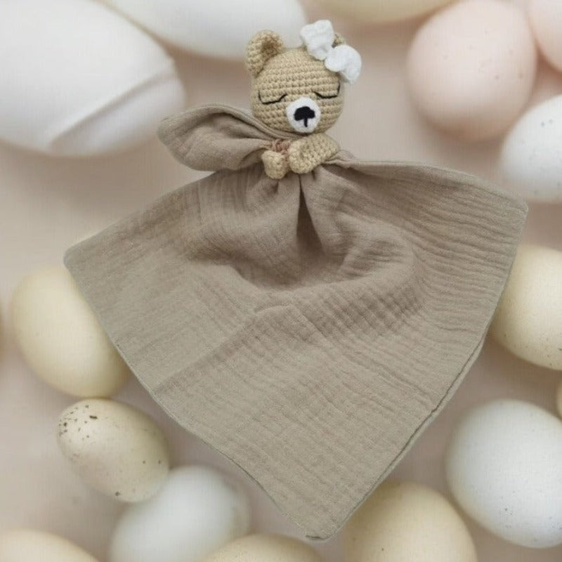 FATIMA est un adorable doudou plat représentant un ours au crochet. Doté d'un noeud blanc sur la tête, il tient un mouchoir ou carré de gaze de coton entre ses pattes pour offrir douceur et réconfort à votre enfant. Disponible en quatre coloris : Écru, Marron, Bleu et Vieux rose. MARRON