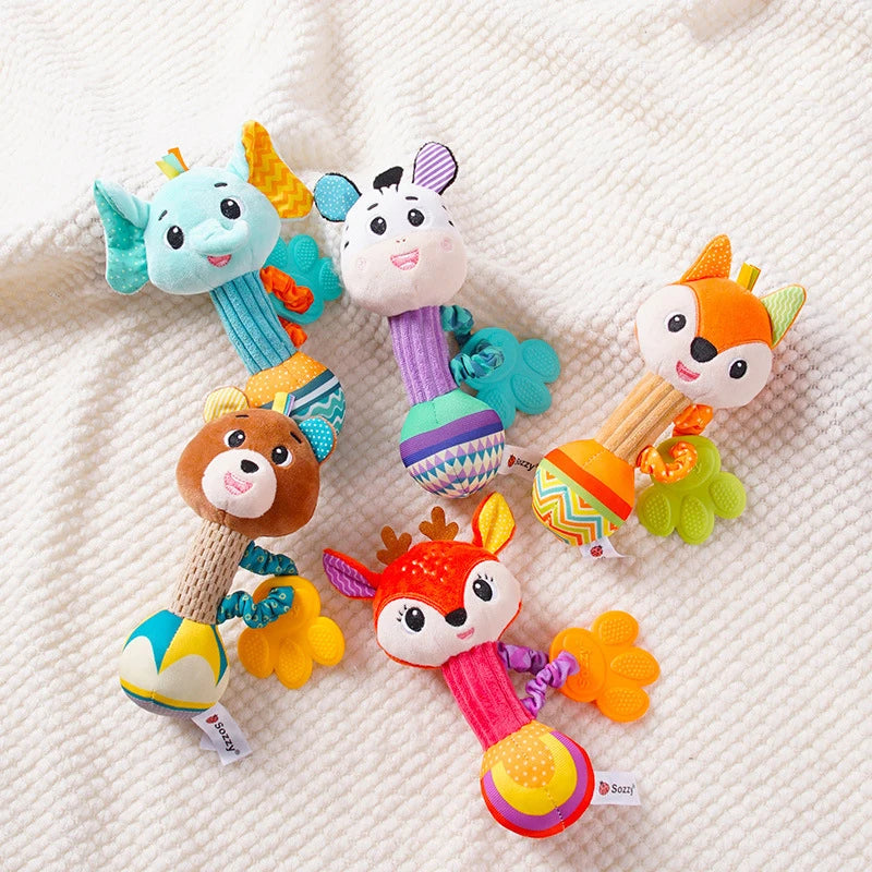 5 Doudou bébé hochet cerf, zèbre, éléphant, ours, renard orange rose violet blanc, bleu, vert, marron, noir et jaune avec anneau de dentition en forme de patte posé sur un tissu cranté clair Image