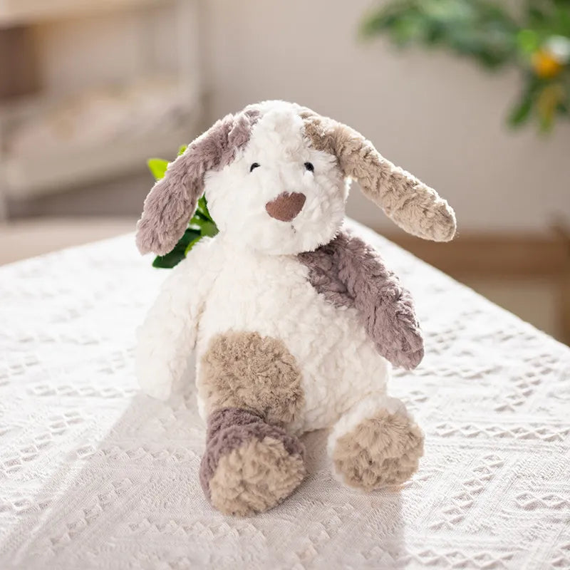 Doudou bébé chien blanc - BONNIE peluche tricolore posée sur un support en tissu blanc avec un fond  flou Image