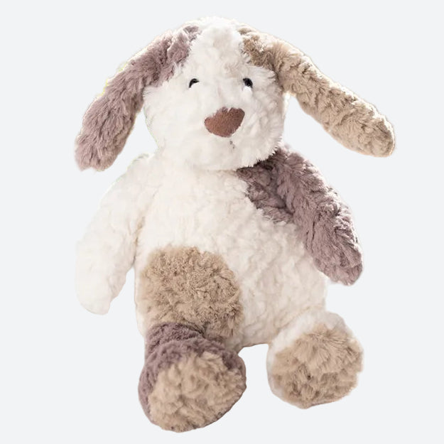 peluche chien tricolore beige blanc et marron posé sur un support en tissu blanc