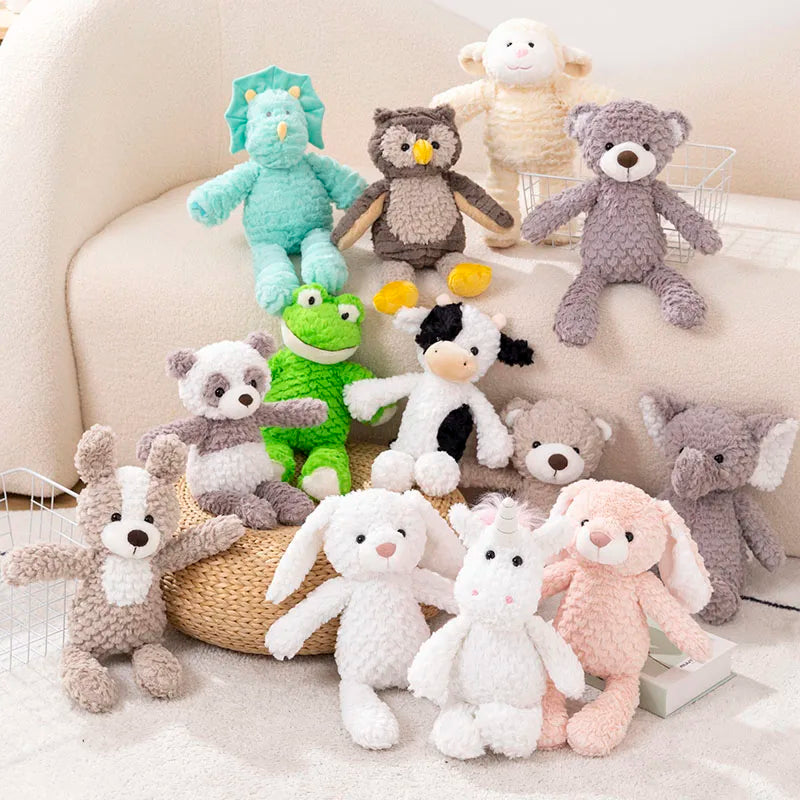 13 peluches animaux, dinosaure, hiboux, mouton, ours, chien, panda, grenouille, vache, lapin, licorne, éléphant mis en scène avec des paniers métalique fin blanc, un divan claire, un livre blanc, un pouf en rotin et un tapin blanc  Modifier le texte alternatif