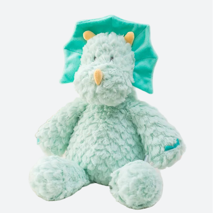 peluche dinosaure bleu posé sur un tissu blanc avec une carte aux motifs floraux à coté