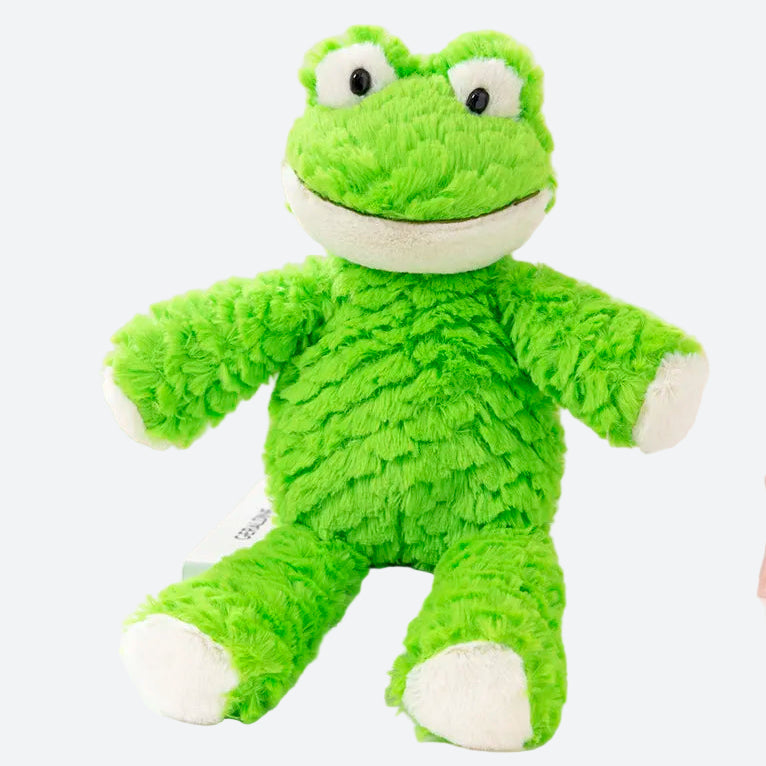 peluche grenouille verte et blanche posée sur un livre bleu ciel . le livre est dans un plateau rond blanc un balle jaune de laine ainsi qu'une lampe rose de bureau se situe également dans ce plateau