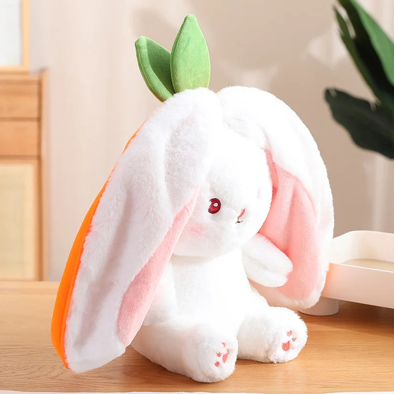 peluche lapin carotte blanc et orage ( en vue 3/4 ) posée sur une table en bois, en fond on peut voir des tiroir en bois sur la gauche et une plante sur la droite