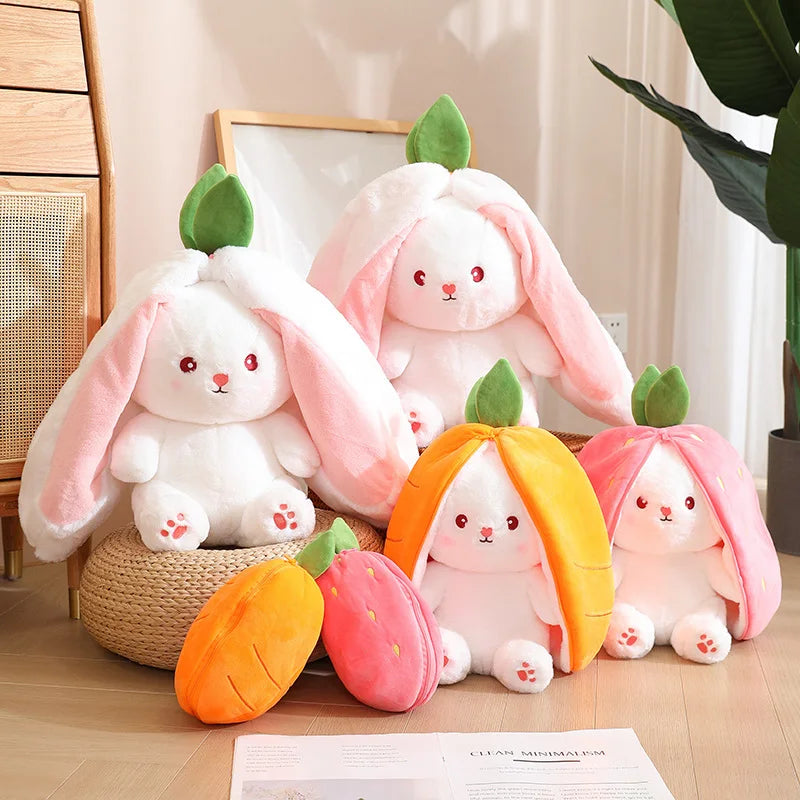 six peluches lapins carottes et fraises posés sur le sol , dont les deux plus gros sont sur des poufs en rotin et les deux plus petits sont zippés fermés. A droite une plante verte est devant une porte vitrée,  à gauche un meuble en bois, derrière un tableau blanc est visible.