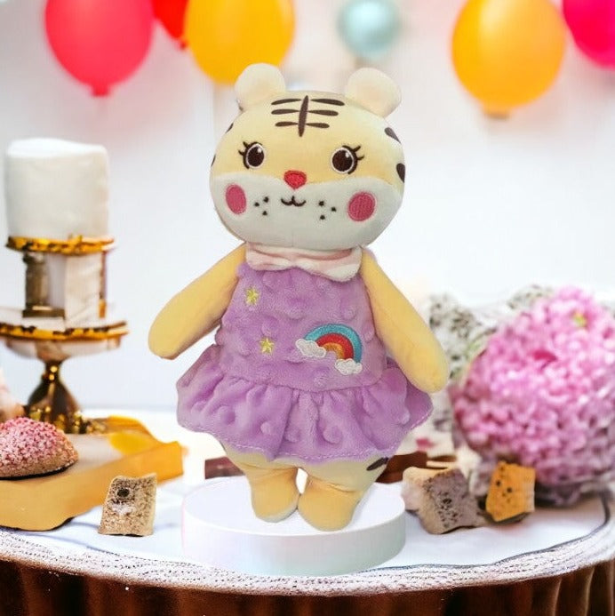 peluche tigre en robe violette avec deux étoiles et un arc en ciel sur la robe. dans un décors de fête.