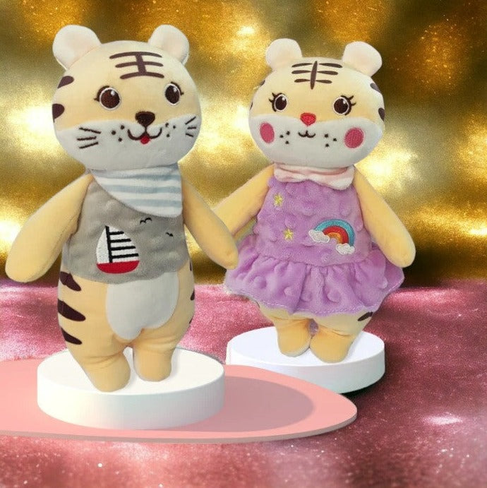 peluche tigre en robe violette avec deux étoiles et un arc en ciel sur la robe aux cotés d'une autre peluche tigre aevc un t-shirt aux airs marins avec un voilier dessiné dessus. Image