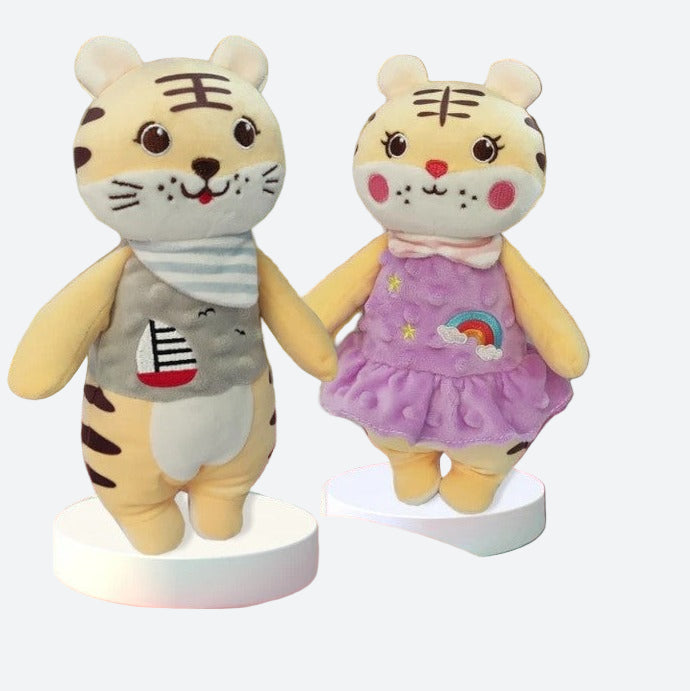 peluche tigre en robe violette avec deux étoiles et un arc en ciel sur la robe aux cotés d'une autre peluche tigre aevc un t-shirt aux airs marins avec un voilier dessiné dessus.