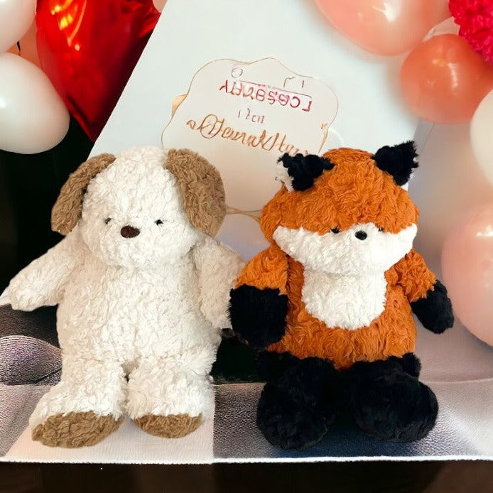 peluche chien blanc et marron aux cotés de la peluche renard orange , blanche et noir