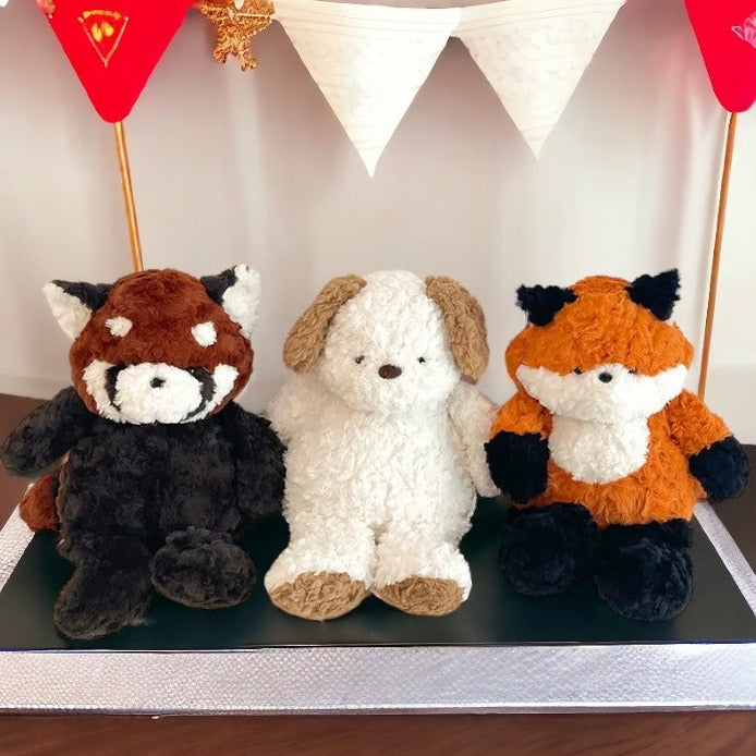 peluche raton laveur marron blanc et noir, peluche chien blanc et marron aux côtés de la peluche renard orange , blanche et noir ( de face )