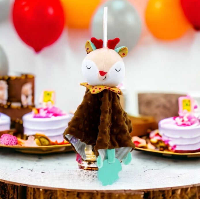 doudou cerf marron à tête beige, aux yeux fermés et aux bois rouge. avec un anneau de dentition bleu en forme de pomme croquée