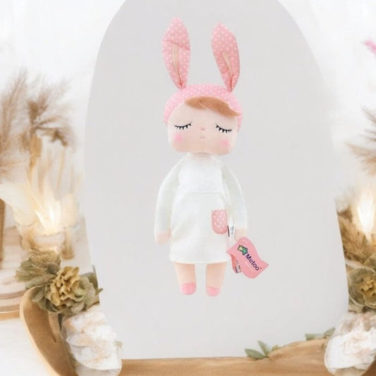 Faites la rencontre de NOVA, le doudou fée dolls de 34 cm, une créature féerique aux oreilles de lapin rose et à la robe blanche ornée d'une poche rose à pois blancs. Avec ses ballerines roses et son sourire radieux, elle est prête à partager son monde merveilleux avec votre enfant.