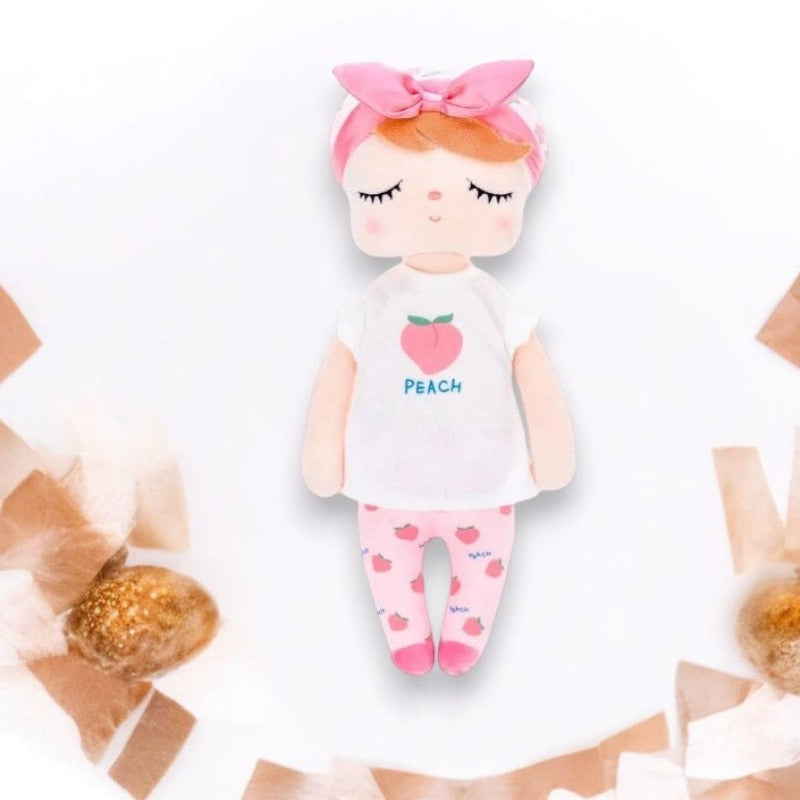 PATY, la fée dolls de 34 cm, émerveille avec son t-shirt blanc orné d'une pêche juteuse, son pantalon rose parsemé de pêches, son bonnet blanc agrémenté de motifs de pêches, son bandeau et ses ballerines roses assorties.