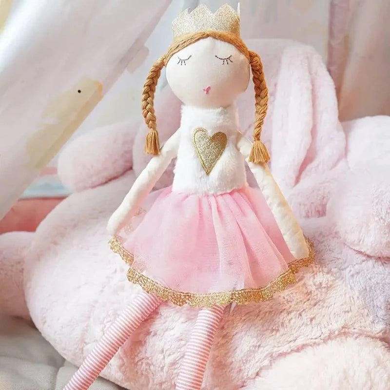 TRISTANIA est une poupée fée de 50 cm, ornée d'une couronne dorée, d'un haut blanc à fourrure avec un cœur doré au centre, d'une jupe tutu rose avec des détails dorés, et de deux tresses élégantes. Image
