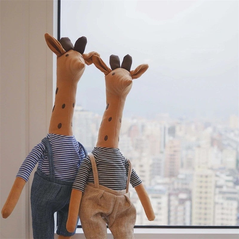 2 doudou girafe habillées devant une fenetre sur la ville