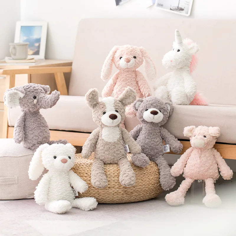 Lapin rose et licorne blanche et rose posées sur le canapé tissu crème et bois clair, devant l’éléphant gris posé sur un pouff gris en tissu, le chien bicolore et l’ours sont posés sur le pouf en rotin à côté, le lapin blanc est posé au sol et le cochon rose est de l’autre côté