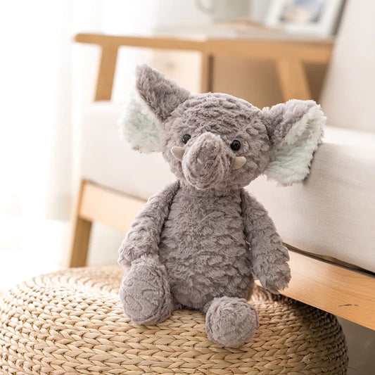 peluche éléphant gris posé sur un pouf en rotin contre un canapé bois et tissu clair 