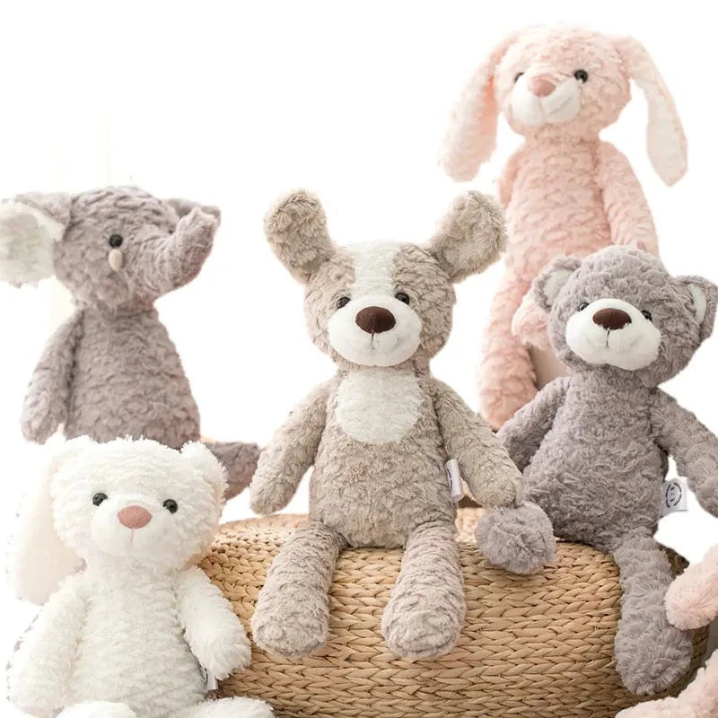 Lapin rose en haut, devant l’éléphant gris, le chien bicolore et l’ours sont posés sur le pouf en rotin à côté, le lapin blanc est posé au sol 