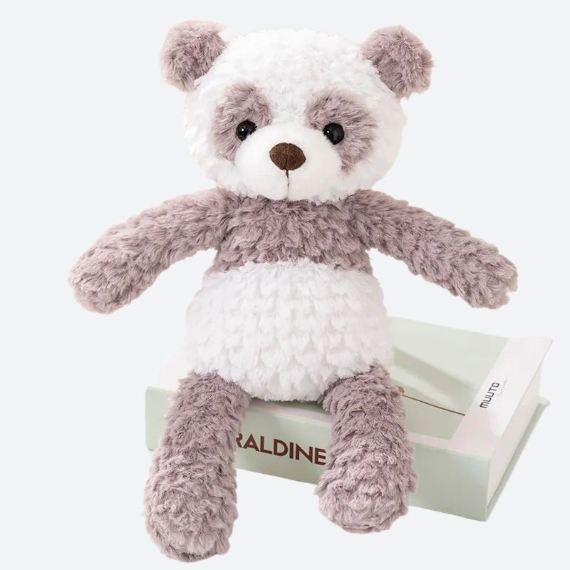peluche panda grise et blanche posée sur un livre blanc, sur un tissu blanc sur une table ronde blanche