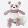 peluche panda grise et blanche posée sur un livre blanc, sur un tissu blanc sur une table ronde blanche