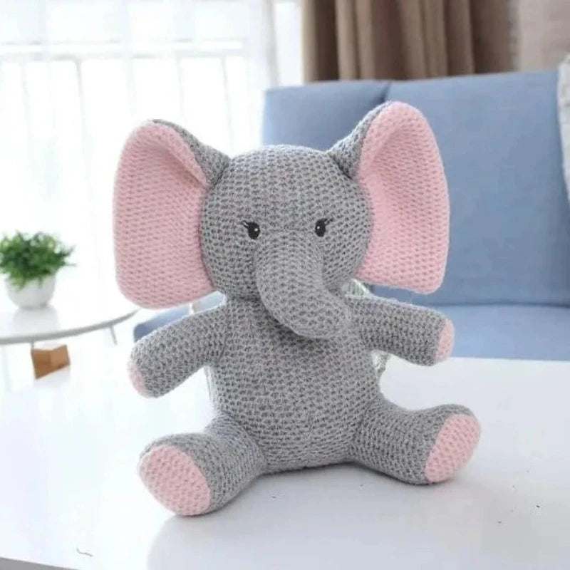  la peluche éléphant UGO. Mesurant 25 cm, cette adorable créature tricotée gris et rose, avec un petit cœur rose sur la poitrine, émerveillera votre enfant par sa tendresse et son charme féérique.