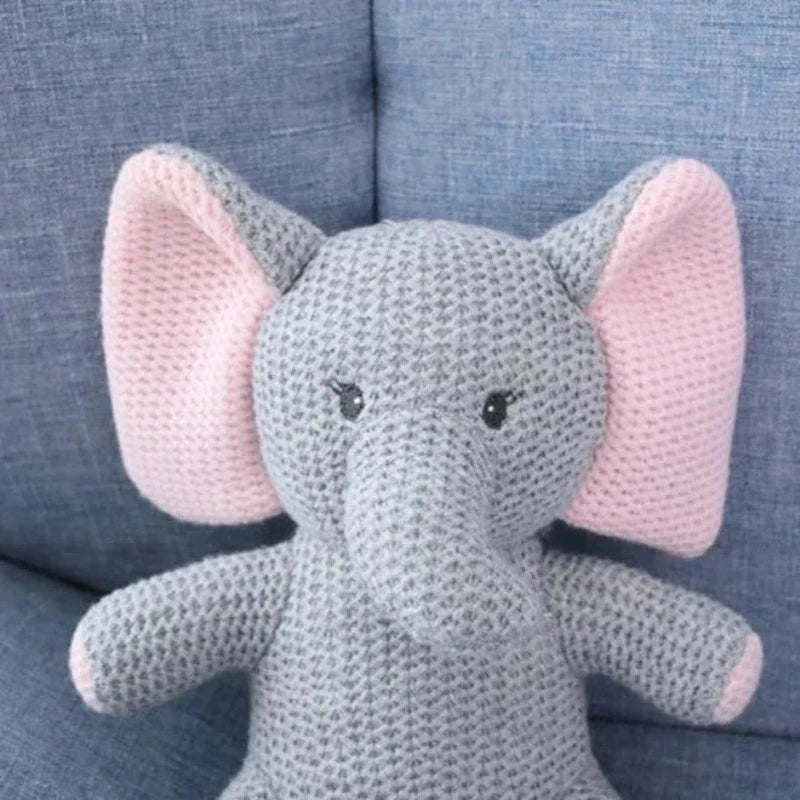  la peluche éléphant UGO. Mesurant 25 cm, cette adorable créature tricotée gris et rose, avec un petit cœur rose sur la poitrine, émerveillera votre enfant par sa tendresse et son charme féérique. zoom sur sa trompe et ses longs cils