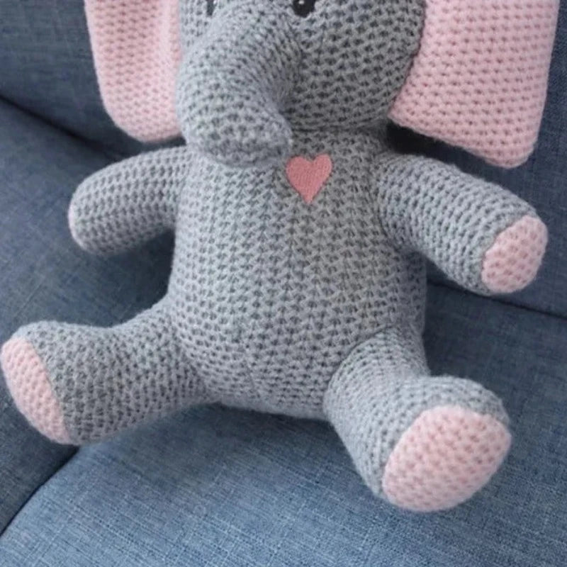  la peluche éléphant UGO. Mesurant 25 cm, cette adorable créature tricotée gris et rose, avec un petit cœur rose sur la poitrine, émerveillera votre enfant par sa tendresse et son charme féérique. Zoom sur le coeur rose sur sa poitrine !