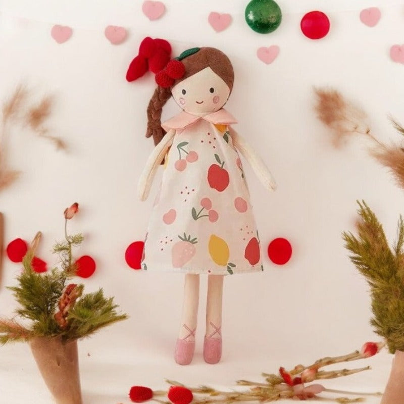 FRUTIYA, la peluche fille de 35 cm, apporte une touche de fraîcheur et de fantaisie avec sa robe aux motifs de fruits et son col Claudine rose. Avec ses cheveux bruns attachés en natte et sa pince cerise, elle est prête à partir à l'aventure !