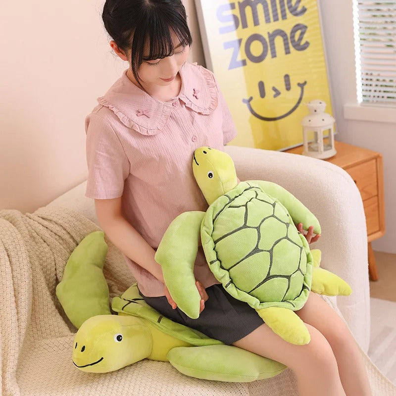 Une femme assise qui tient la eluche tortue verte - Sally et qui est assise sur une autre peluche tortue
