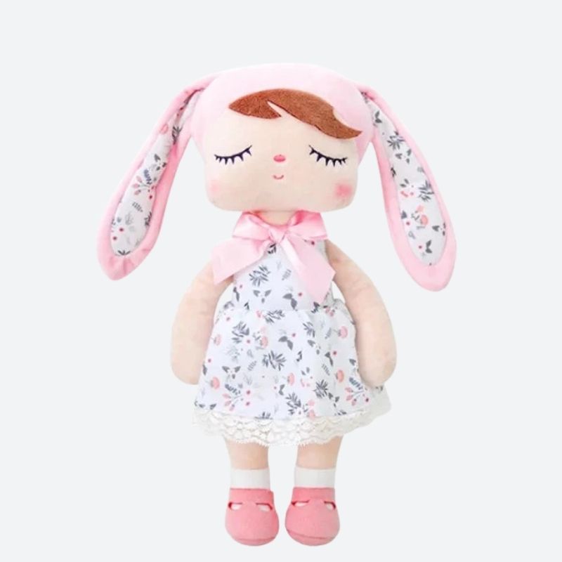 SURI, la fée dolls de 34 cm, éblouit avec sa robe blanche à fleurs, son bonnet à oreilles de lapin rose et blanc assorti, et ses ballerines roses, créant ainsi un tableau enchanté digne des contes de fées.