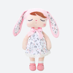 SURI, la fée dolls de 34 cm, éblouit avec sa robe blanche à fleurs, son bonnet à oreilles de lapin rose et blanc assorti, et ses ballerines roses, créant ainsi un tableau enchanté digne des contes de fées.