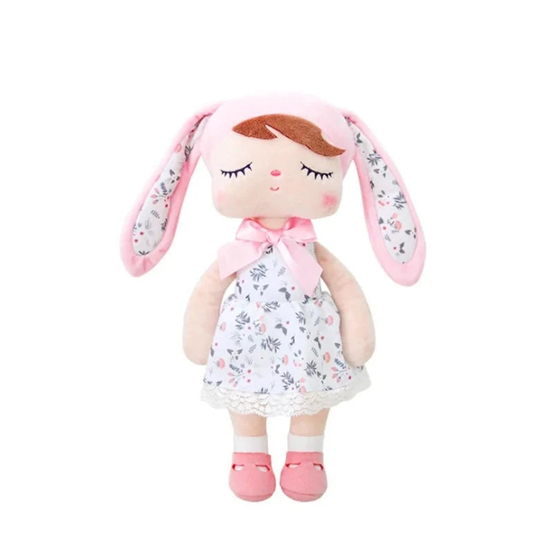 SURI, la fée dolls de 34 cm, éblouit avec sa robe blanche à fleurs, son bonnet à oreilles de lapin rose et blanc assorti, et ses ballerines roses, créant ainsi un tableau enchanté digne des contes de fées.