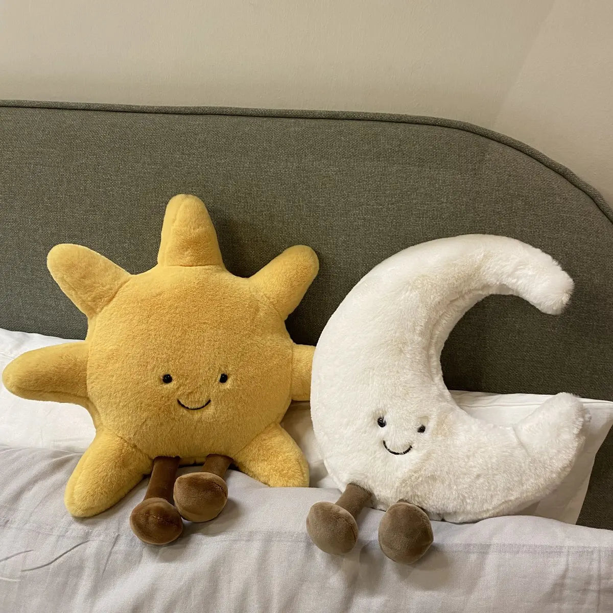 peluche lune souriante blanche avec peluche soleil jaune souriant, dans un lit