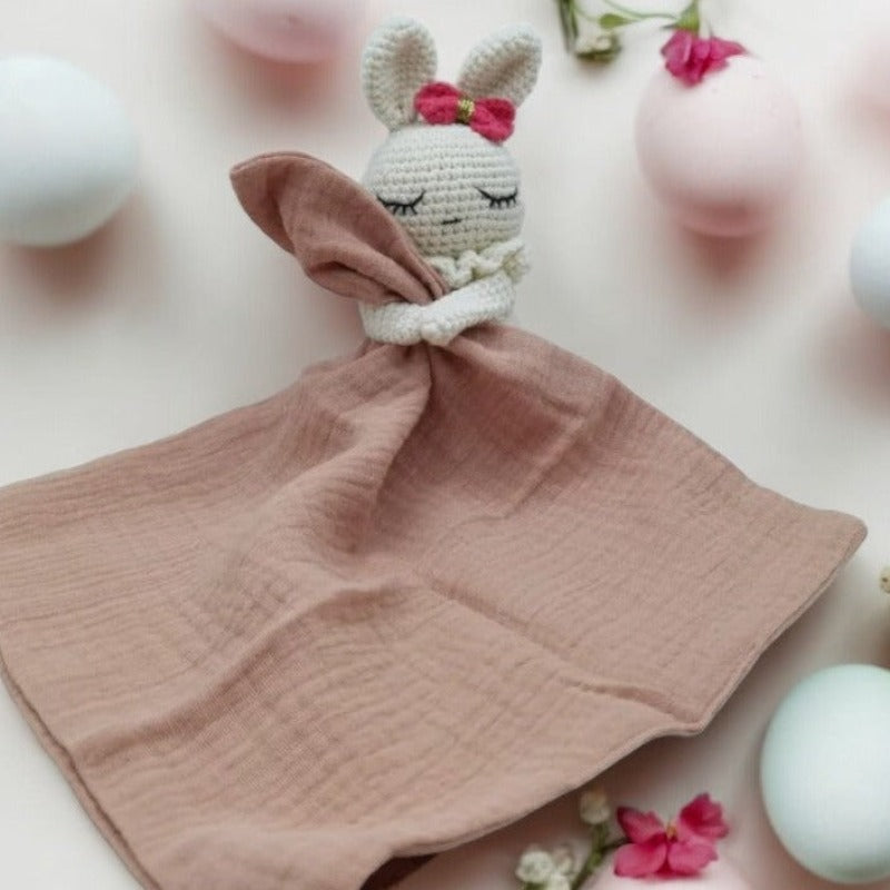 LIVIA est un adorable doudou plat représentant un lapin au crochet. Avec son noeud rose et doré sur la tête, il tient un mouchoir ou carré de gaze de coton entre ses pattes pour offrir douceur et réconfort à votre enfant. Disponible en trois coloris : Écru, Rose pâle et Vieux rose. VIEUX ROSE